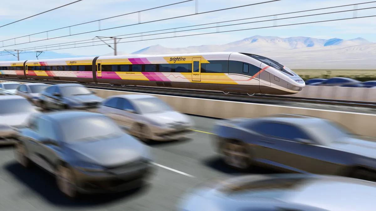 A Brightline train in white, yellow and pink colors races along a track under electric wires while blurred cars are seen on a highway in the foreground.