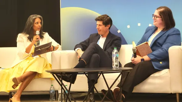 Three people sit on a couch. The person on a left, in a yellow dress, speaks.