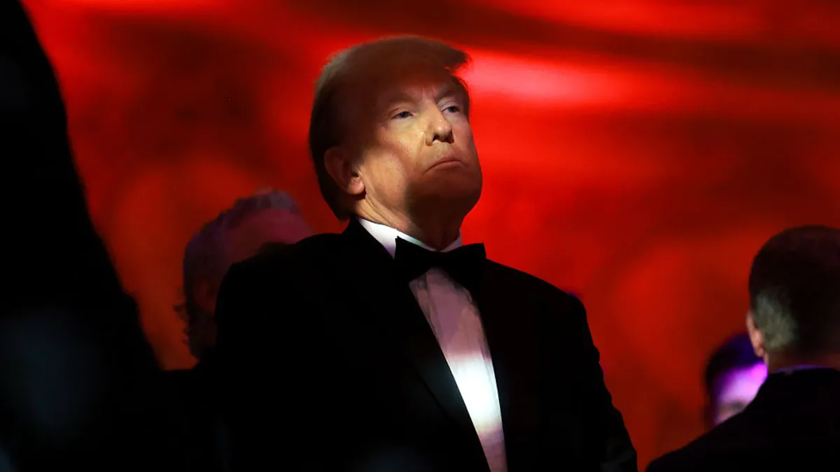 Donald Trump stands against a red backdrop with a shadow over his face