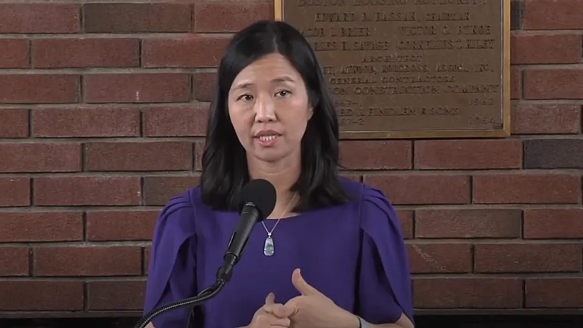 A person speaking into a microphone in front of a brick wall