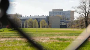A large commercial building with a green grass lawn is framed through a wire metal fence mesh. National Institutes of Standards and Technology in Gaithersburg, Md., on April 17, 2022.