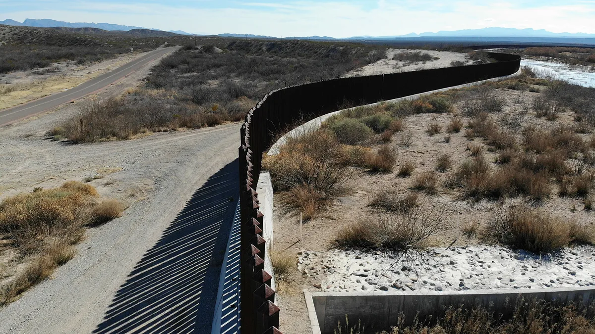 A simple dark metal fence snakes through a desert landscape.