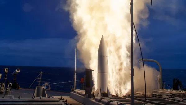 A missile fired up to launch from a deck of a ship at night.