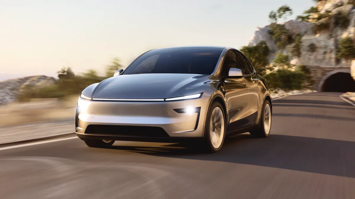 A gray 2026 Tesla Model Y driving on a road with a tunnel in the background.