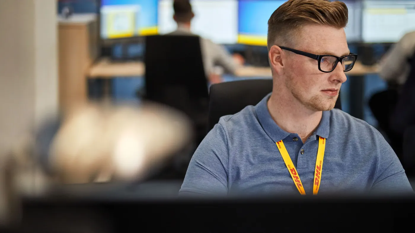 A DHL employee sits in front of a computer.