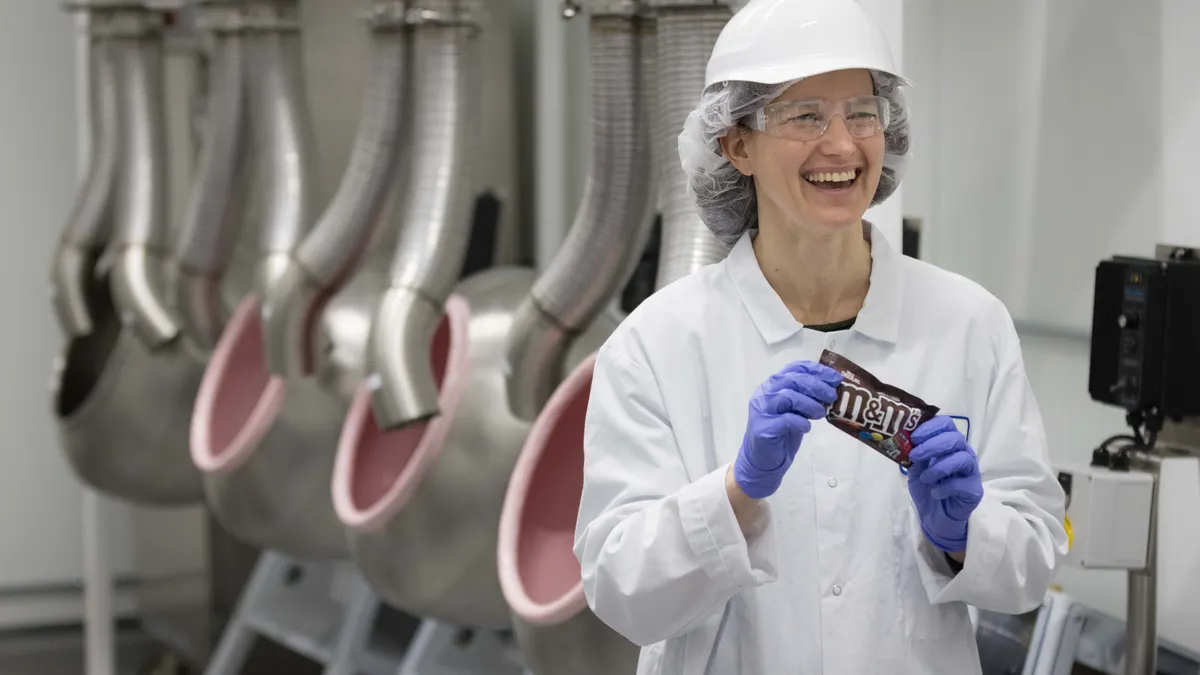 Factory worker standing in front of equipment holding a M&Ms candy package