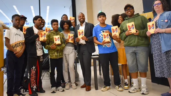 A group of people are standing in a library holding the same book.