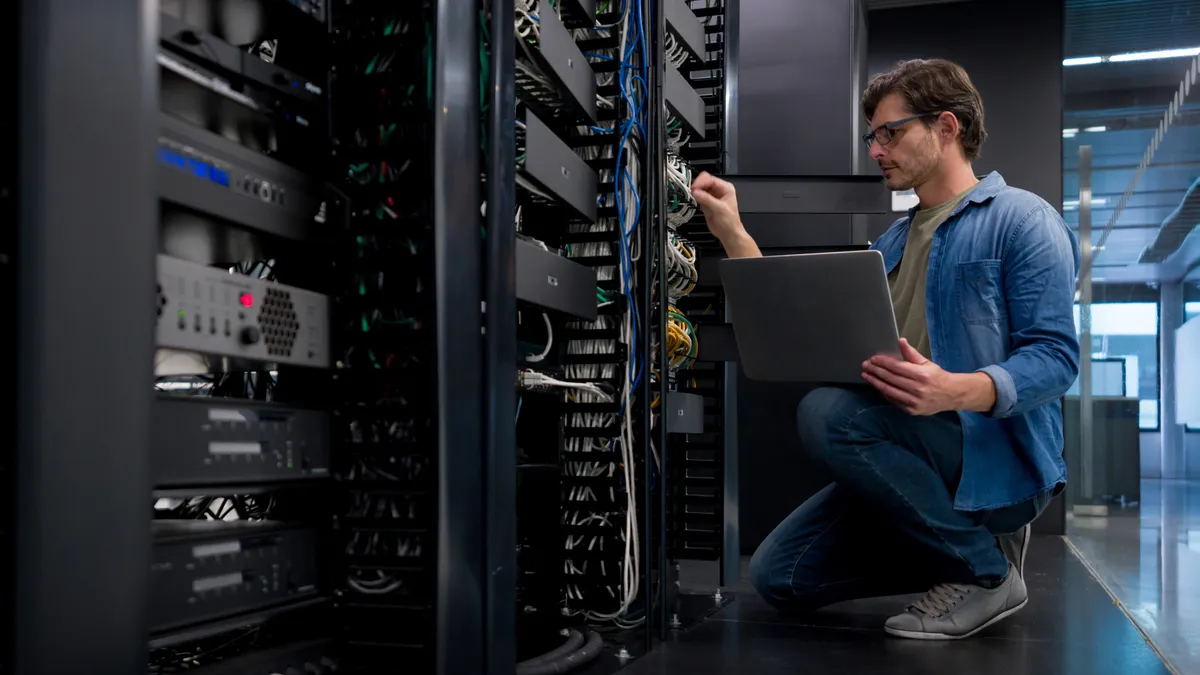 A technician kneels down to inspect a rack of computer servers.