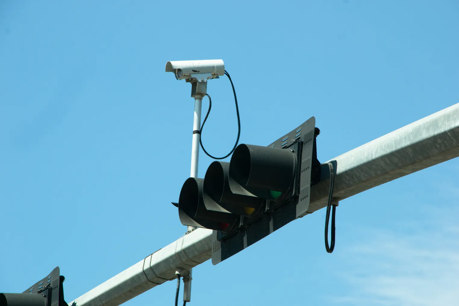 A traffic signal mounted horizontally on an overhead arm next to a camera.