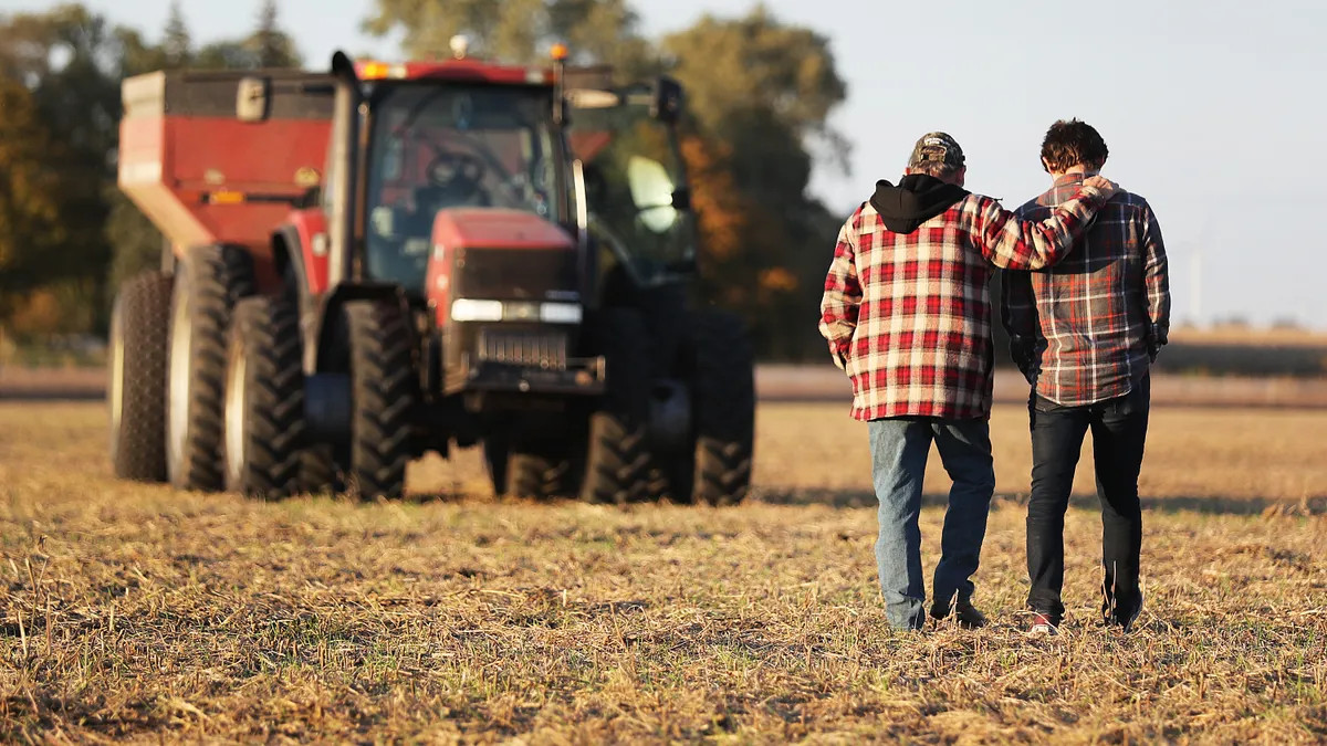 A farmer and his son walk toward a tractor with their backs to the camera.