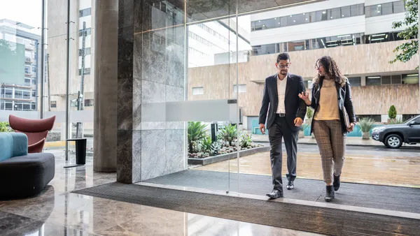 Two coworkers walk into a modern office building.