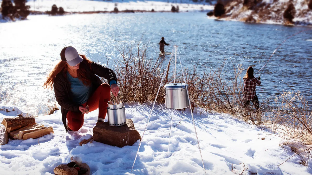 A person tends a fire on a patch of land covered in snow.