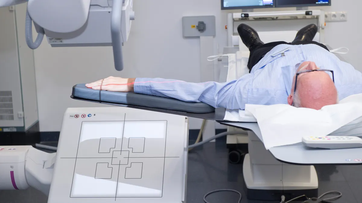 A person lays with their arm outstretched and an x-ray camera facing it.