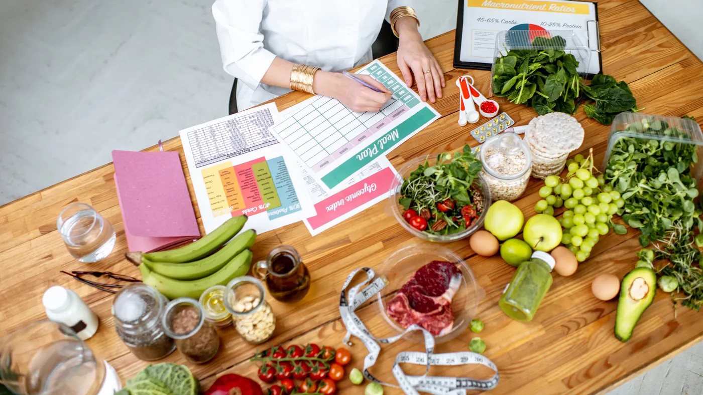 Dietitian writing a diet plan, view from above on the table with different healthy products and drawings on the topic of healthy eating.