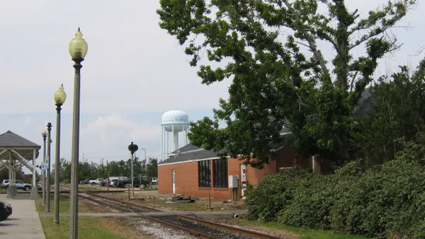 A red brick building alongside a railroad track and a station platform on the opposite side and a water tank label "Gulfport" in the background.