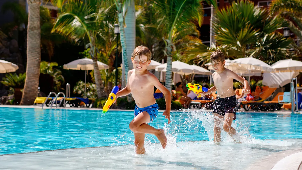 Two children play with squirt guns at a hotel pool.