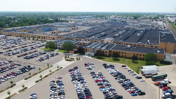 A large brown and black facility with a parking lot with cars in front of it.