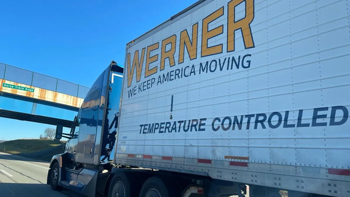 A Werner tractor-trailer approaches an underpass on an interstate.