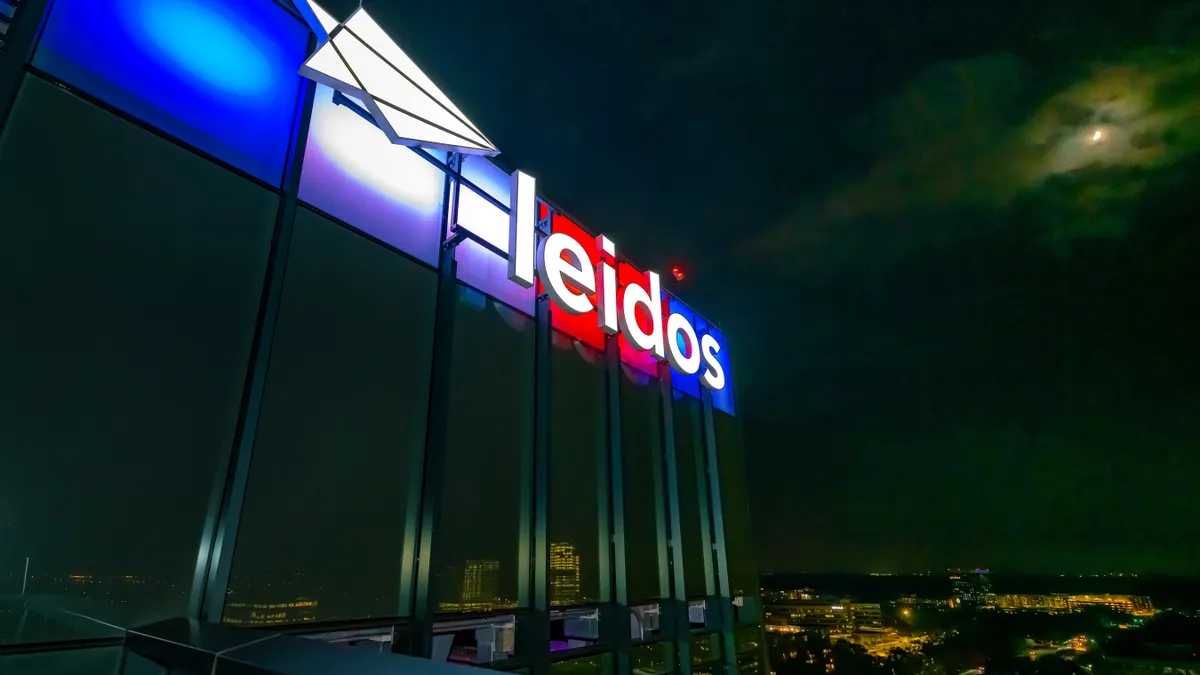 A white Leidos logo sign on a building, being back lit with red, white and blue lights.