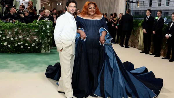 A man in a white suit and a woman in a blue denim gown stand in front of photographers.