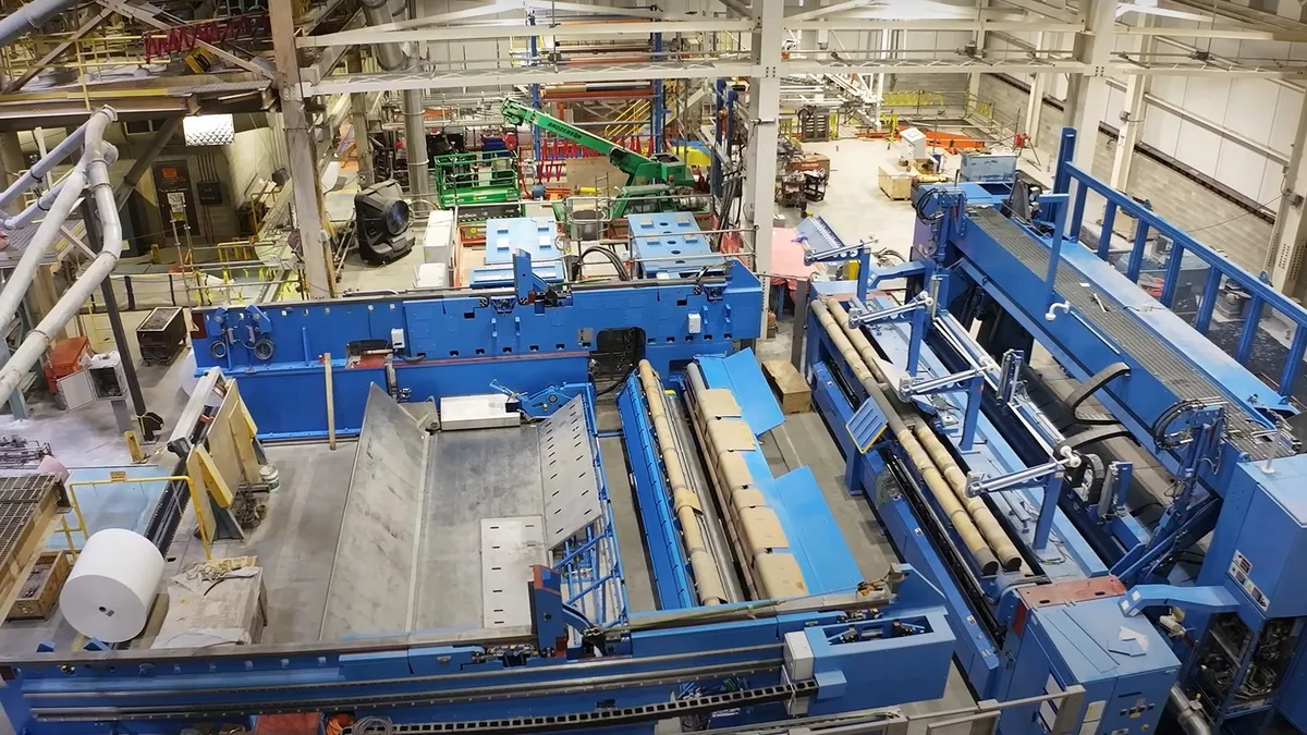 A large roll of white paper is next to industrial equipment in a manufacturing facility.