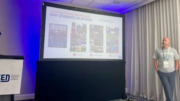 A high school teacher stands to the right of a screen while presenting on a student public relations program.