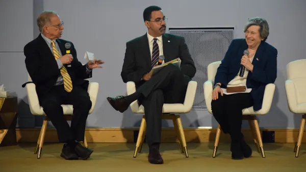 Three people are sitting in chairs on a stage. One person has a microphone