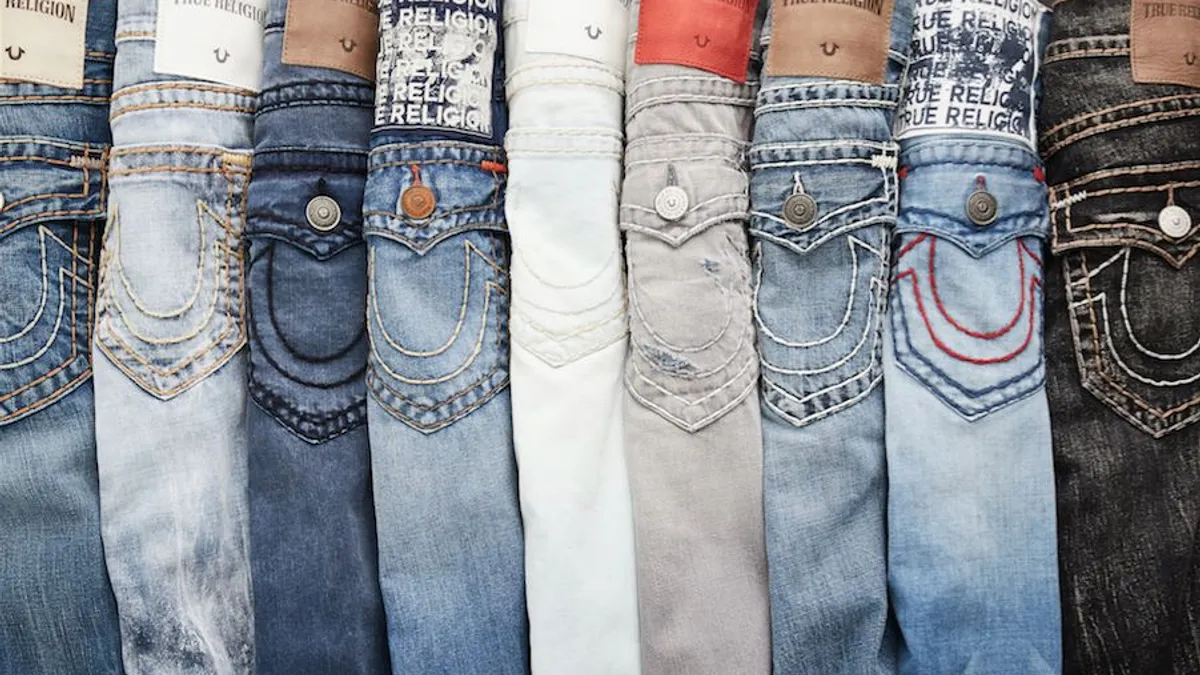 A line up of nine folded pairs of jeans in various shades with the True Religion brand label showing.