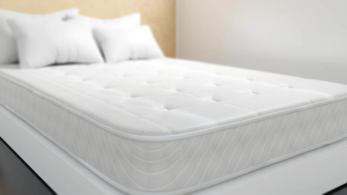 Picture of a white mattress with pillows on top, sitting on top of a white bed frame.