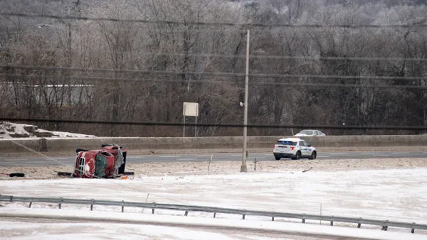 A red pickup on its side with a police car a short distance ahead on a highway.