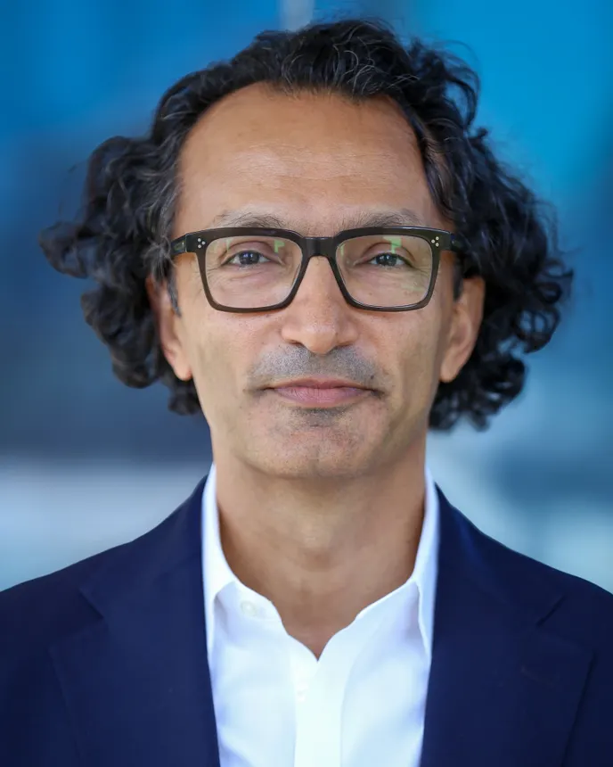 Head shot of man with glasses wearing a blue suit over a white shirt.