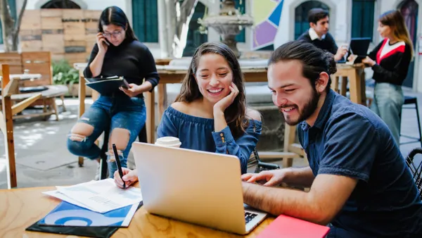 two people sitting at a table looking at a laptop