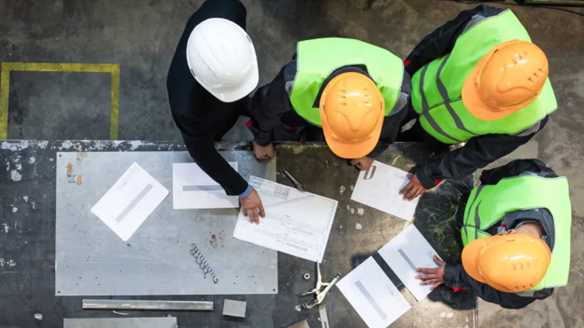 Three men in hard hats and safety vests discussing blueprints at a table.