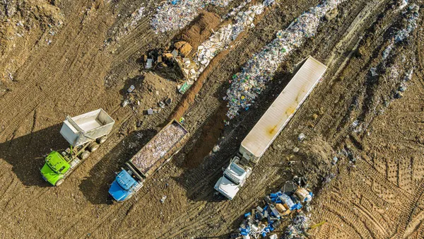 An aerial view of three waste trucks in a landfill site; the surrounding area contains waste and dirt. 