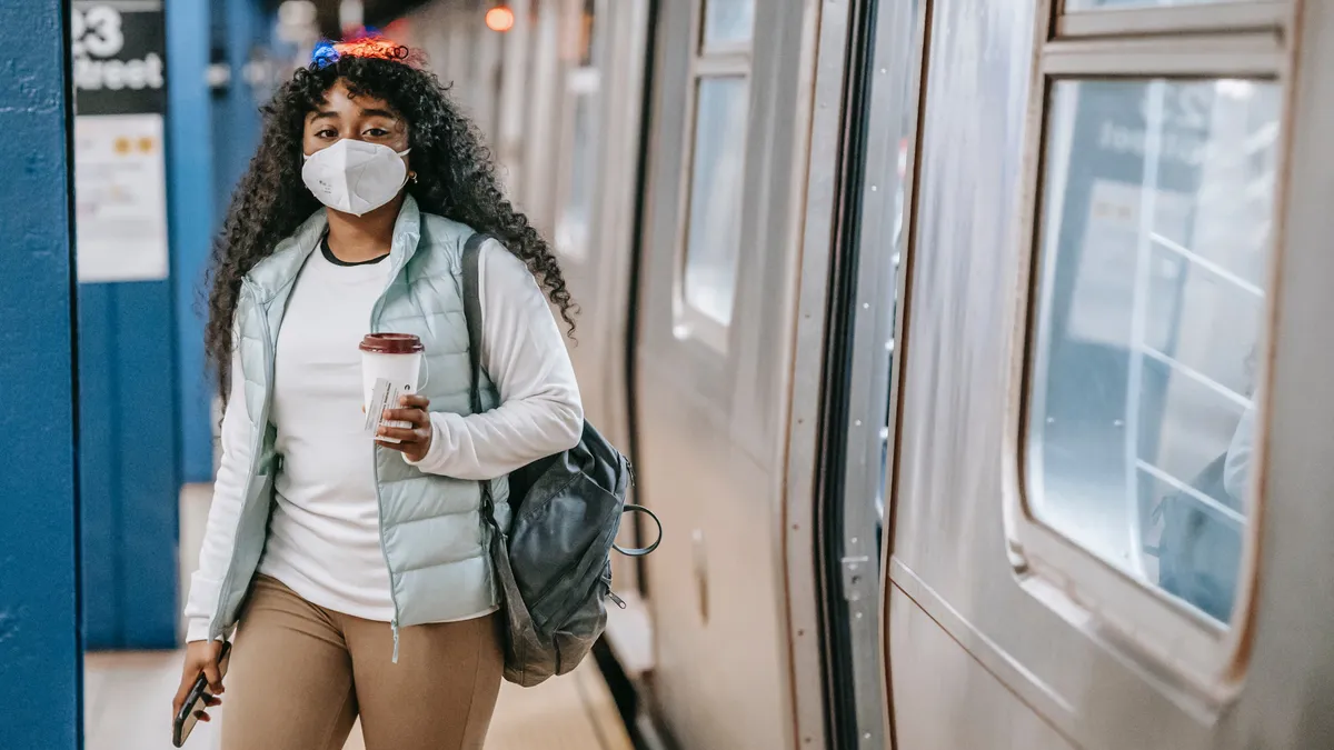 Person with medical mask stands by train with coffee