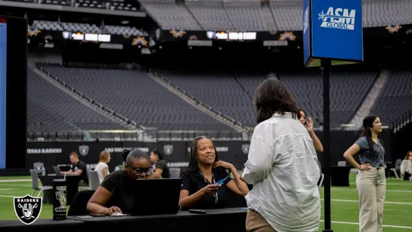 Job seeker stands in front of two women at a table, against the backdrop of sports stadium seating.
