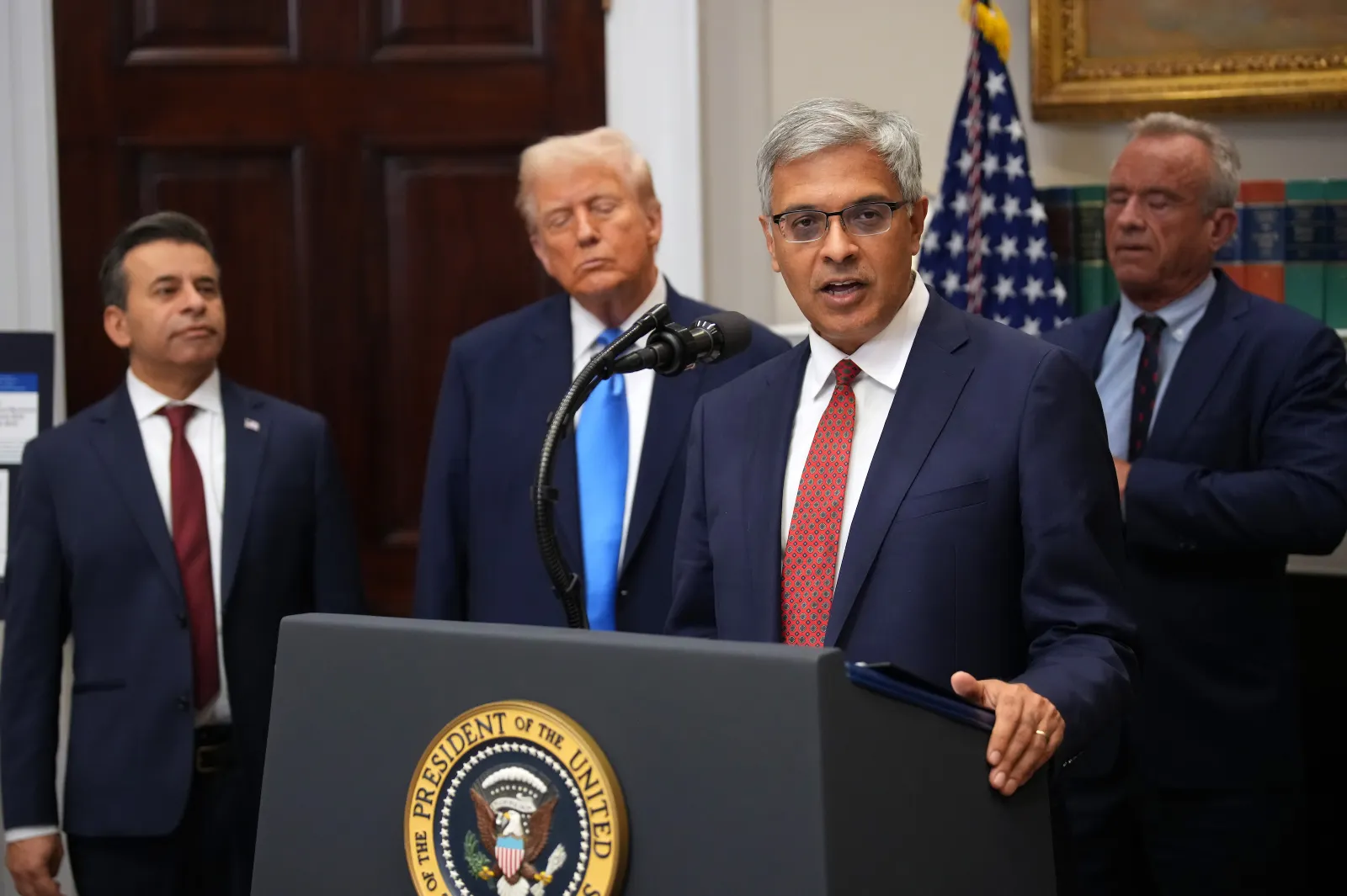 Four people wearing blue suits stand behind a podium.