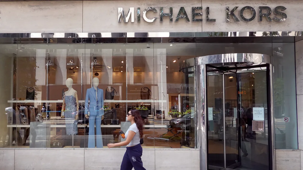 A person walks in front of a Michael Kors storefront.