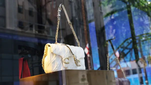 A white Coach bag with a gold chain strap is displayed in a store window.