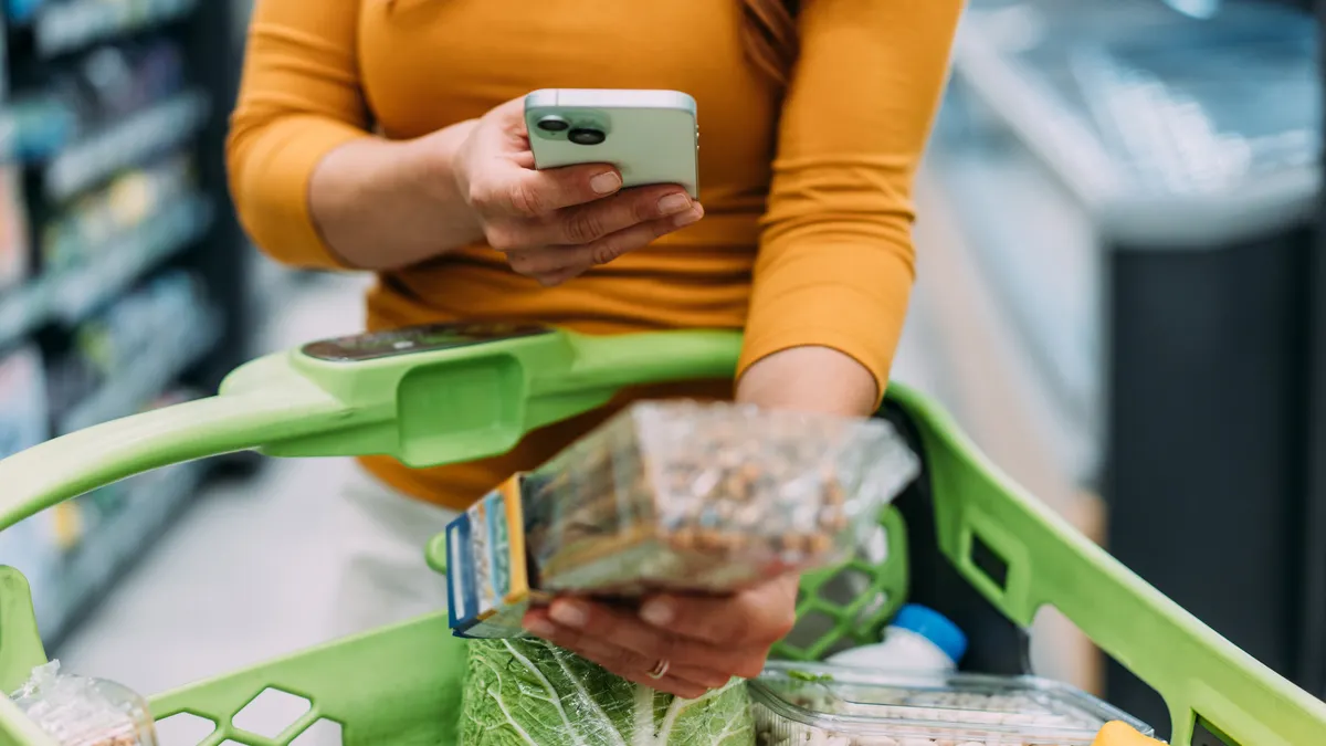 Woman scans food label in front of a shopping cart