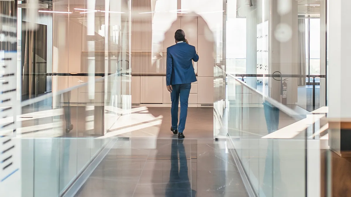 A person wearing a blue business suit walking down a skyway with glass windows.