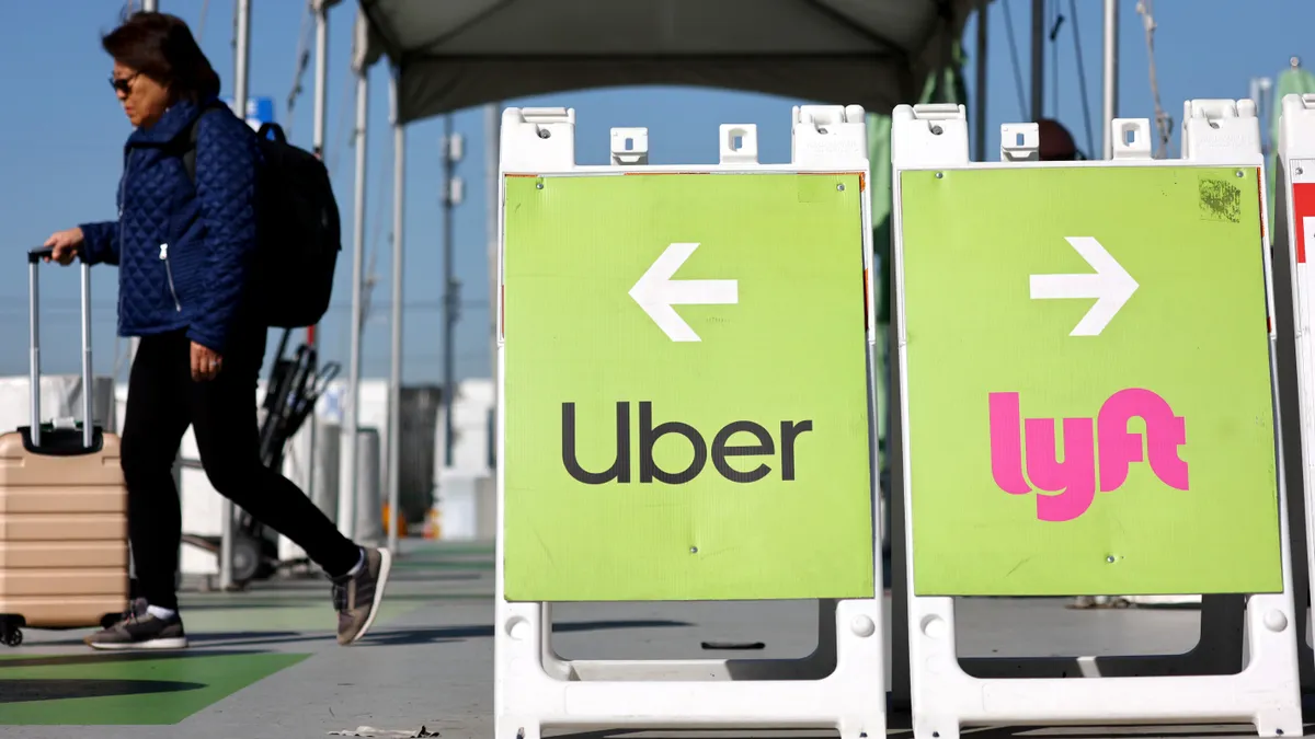 A woman with rolling luggafe walks near Uber and Lyft signs.