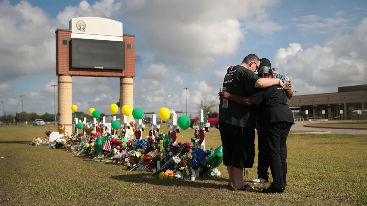 Mourners huddle around a memorial in front of Santa Fe High School