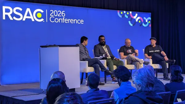 Four men sit on a stage in front of an audience. Behind them, a blue backdrop displays a logo reading "RSAC 2026 Conference."