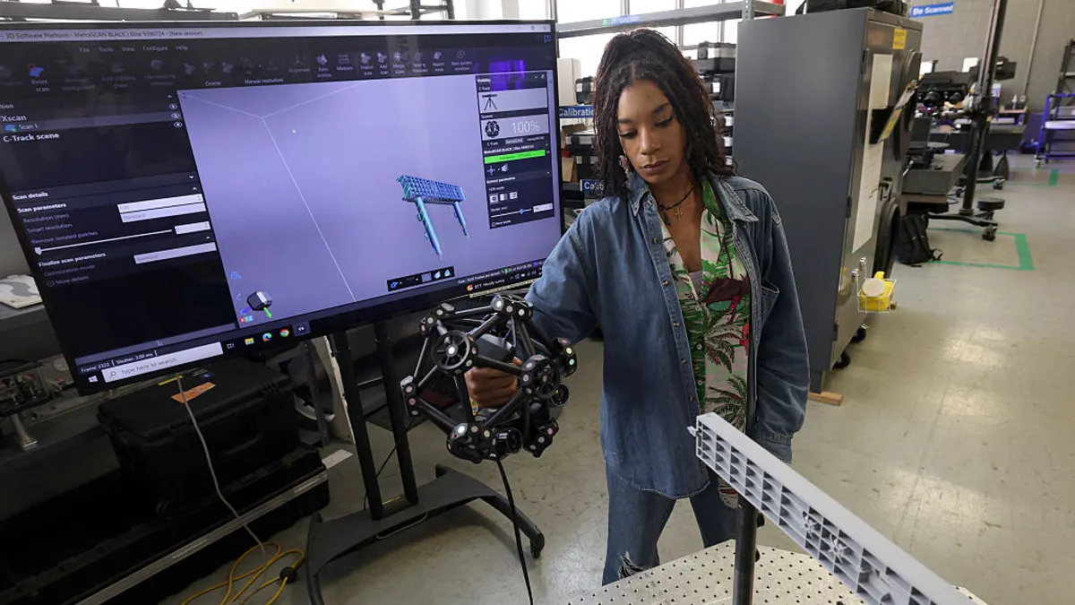 A woman holds a 3-D lab apparatus in her right hand. A screen is behind her depicting as aspect of a 3-D model.