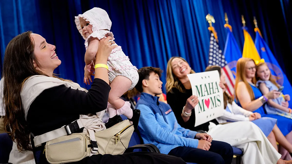 A woman holds a sign that says "MAHA Moms" next to another woman holding a baby.