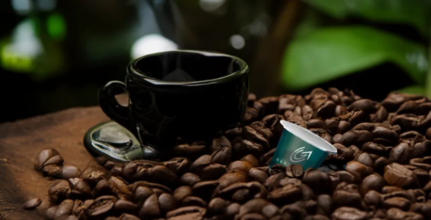 A coffee cup and coffee pod lie on spread out coffee beans.