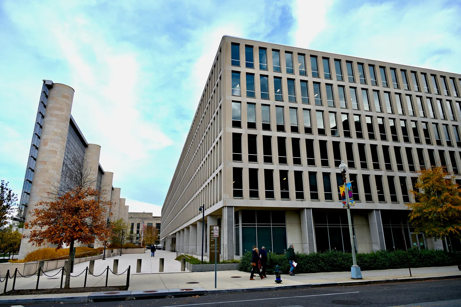 The outside of the U.S. Department of Education in Washington, D.C. is shown on a close day. People are walking on the sidewalk in front of the building.