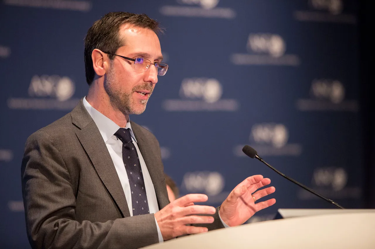 A person in a business suit speaks at a lectern.