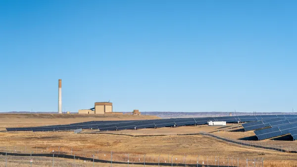 Solar panels in a field next to a coal-fired power plant.